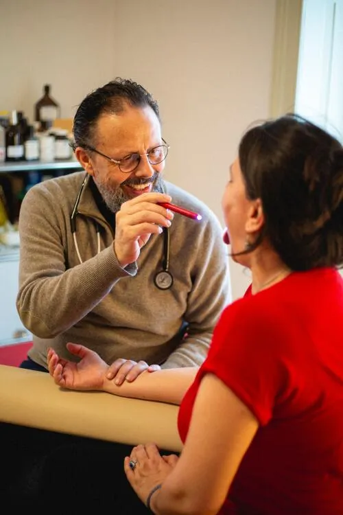 A practitioner examines a patient's tongue using a penlight during a holistic health consultation.