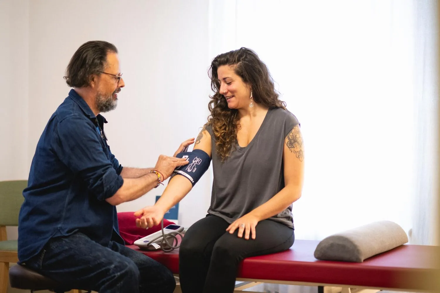 A doctor places a blood pressure cuff on a smiling female patient's arm during a check-up.