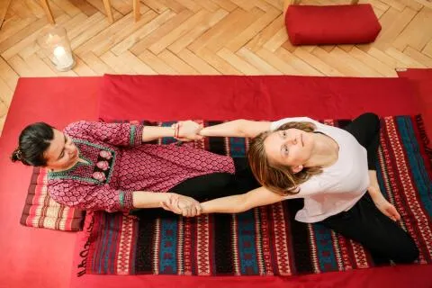 Practitioner performing an assisted upper body stretch during a Thai massage session on a floor mat.