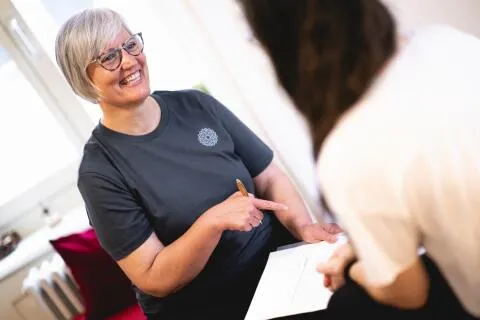 A smiling wellness coach discusses health notes on a document with a client during a consultation.